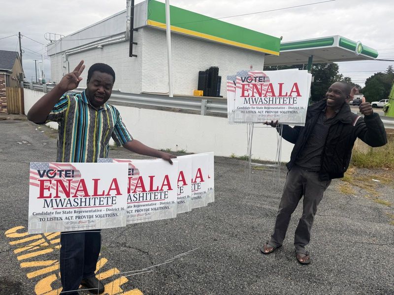 Two campaign volunteers smiling and holding Vote! Enala Mwashitete yard signs.